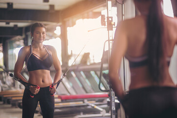 Happiness woman exercise with cable weight machine in front of mirror at fitness gym. Selected focus	