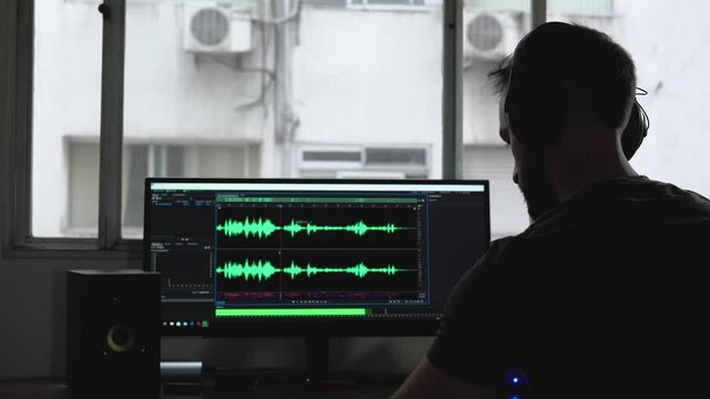 Man editing music in computer in home recording studio, silhouette back view