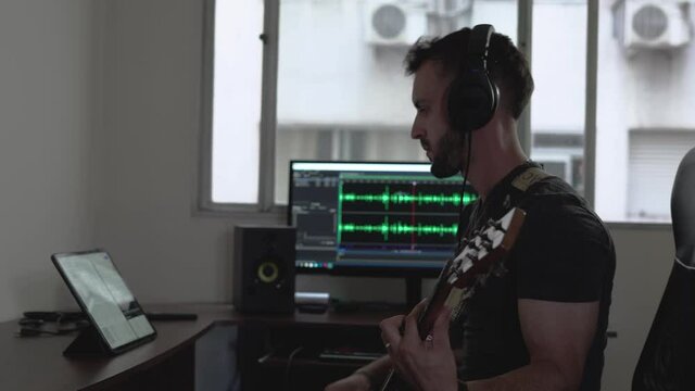 Young Man Playing Guitar And Using IPad In Home Recording Studio