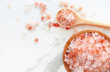 top view of himalayan pink rock salt in wooden bowl and spoon on white marble table.