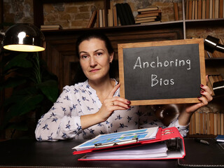 Woman wearing blue business suit and showing black chalkboard with written text Anchoring Bias .
