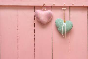 Composition for Valentine's Day. Two fabric hearts hang on jute rope against background of pink wooden wall. Concept of love, wedding, tenderness. Copy space, place for your text