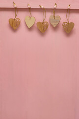 Many small hearts carved from wood hang pinned to pink wooden background. Copy space, place for your text. Valentin's day concept, love, wedding