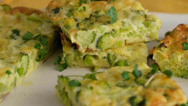Close-up camera movement. Frittata with broccoli on a plate. Italian breakfast. Baked chopped omelet with vegetables and broccoli on a serving plate and sets it on the table. Healthy breakfast.