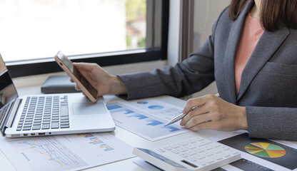 Asian female employees are analyzing market data via smartphones and have laptops to calculate the company's finances In a private office at home, Working at home and new normal concept.