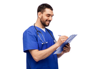 healthcare, profession and medicine concept - happy smiling doctor or male nurse in blue uniform writing medical report on clipboard over white background