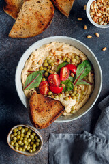 Hummus with green pea, pine nuts, tomatoes and swiss chard. Vegetarian healthy dish, top view.