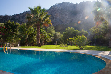 Beautiful sunny view of swimming pool, garden with palm trees and mountains. 