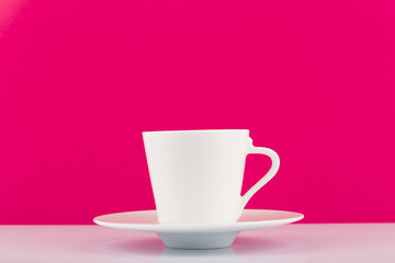 White ceramic coffee cup with saucer against pink background with copy space