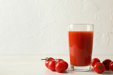 Glass of tomato juice and tomatoes on white textured background