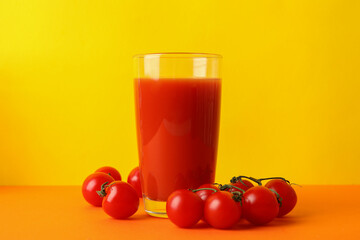 Glass of tomato juice and tomatoes against yellow background