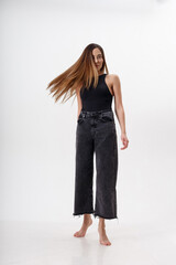 portrait of young attractive asian woman with long hair in black bodysuit, jeans, isolated on white studio background. skinny pretty female posing on cyclorama. model tests of beautiful lady