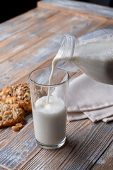 Fresh cow milk is pouring from a bottle into a glass, of oat cookies aside. Beautiful country atmosphere for a magazine