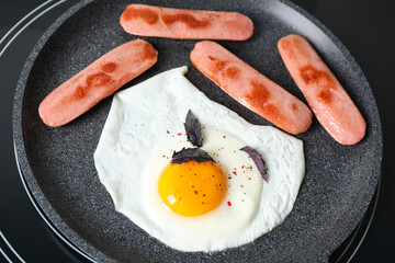 Egg and sausages in frying pan on stove, closeup