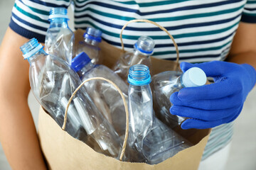 Woman holding paper bag with used plastic bottles indoors, closeup. Recycling problem