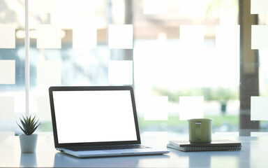 Mock up laptop computer with blank screen, coffee cup and notebook on modern workspace.