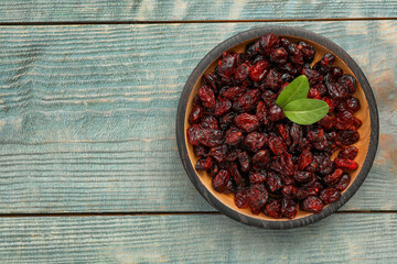 Tasty dried cranberries and leaves in bowl on blue wooden table, top view. Space for text
