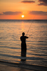 A man fishing in the Indian ocean with the beach at sunset
