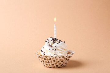 Delicious birthday cupcake with candle on beige background