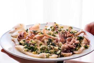 Delicious dish of grilled squid with garlic and parsley on a pale white background