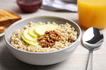 Tasty oatmeal porridge with walnuts and apple slices on white wooden table, closeup