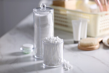 Cotton buds and pads in transparent holders on white marble table