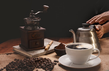 Steam coffee cup with grinder, roasted beens,coffee ground and kettle over burlap hessian  on grunge wood table background