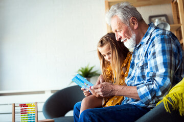 Bearded grandfather and his grandchild are having fun reading a book together