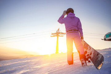 Snowboarder woman with snowboard stands on ski lift snow mountains sunset