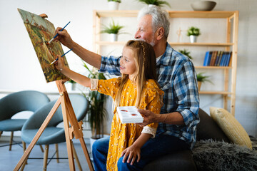 Senior man with child painting on canvas. Grandfather spending happy time with granddaughter.