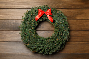 Christmas wreath made of fir branches with red bow on wooden background, top view