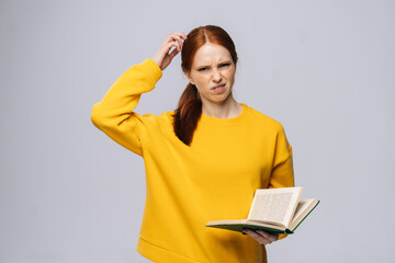 Doubtful dissatisfied young woman college student wearing yellow sweater looking at camera holding...