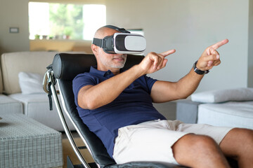 uomo vestito casual gioca con la tecnologia virtuale grazie ad un visore nel salotto di casa