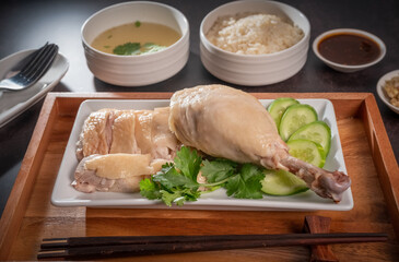 Steamed chicken and rice with spicy sauces and chicken soup, Hainanese chicken rice on a black table background, 