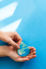 Woman hand holding paper cut water drop on blue background. Clean water and sanitation, saving water. World Water Day. Ecology concept.