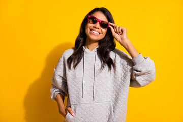Fototapeta premium Photo of positive happy dark skin young woman hold hand pocket hoodie isolated on yellow color background