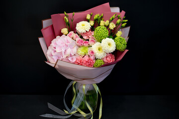 A bouquet of fresh flowers in decorative packaging. Photo on a dark background. Congratulatory bouquet.