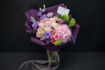 A bouquet of fresh flowers in decorative packaging. Photo on a dark background. Congratulatory bouquet.