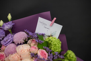 A bouquet of fresh flowers in decorative packaging. Photo on a dark background. Congratulatory bouquet.