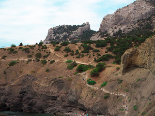 A stone slope of a mountain with a hiking trail, along which tourists walk. Beautiful mountain landscape.