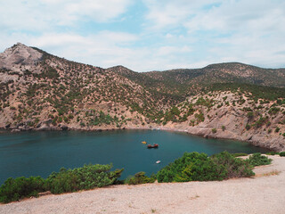 A beautiful sea bay with greenish water and a beach where people relax. Quiet sailboats. Mountain landscape.