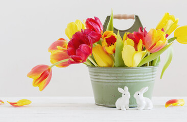 red and yellow tulips in bucket and ceramic rabbit on white background