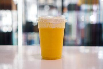 A plastic cup of mango smoothie topped with cheese cream. Separated layer.