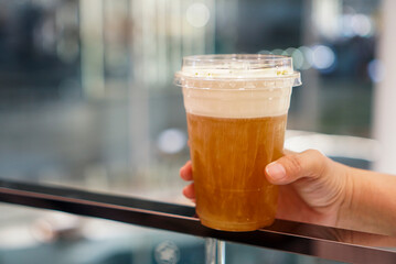 Woman holding a plastic cup of tea topped with cheese cream. Copy space.