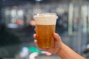 Woman holding a plastic cup of tea topped with cheese cream. Center.