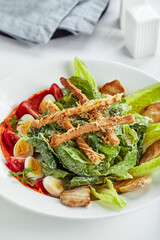 Caesar salad with bread sticks, quail eggs, cherry tomatoes and grilled chicken in plate on white background