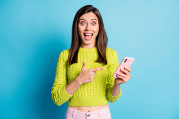 Photo of young happy positive smile girl recommend choice advice point index finger smartphone isolated over blue color background