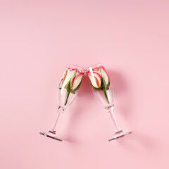 Toast with champagne glass with rose flowers against pastel pink background. Minimal love or season party concept. Nature bloom idea. Flat lay, top view, copy space.