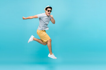 Energetic happy young Asian man jumping studio shot isolated in light blue background