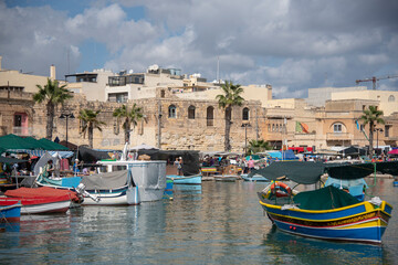 Barcos tipicos de colores con edificios marrones en el fondo en el pueblo llamado Marsaxlokk en Malta. 